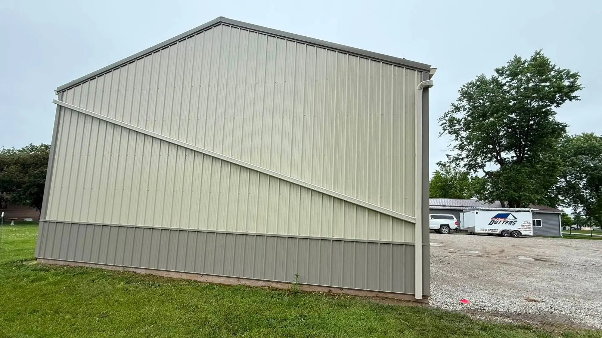 Cream pole barn with a new gutter and downspout, the company trailer parked in the background