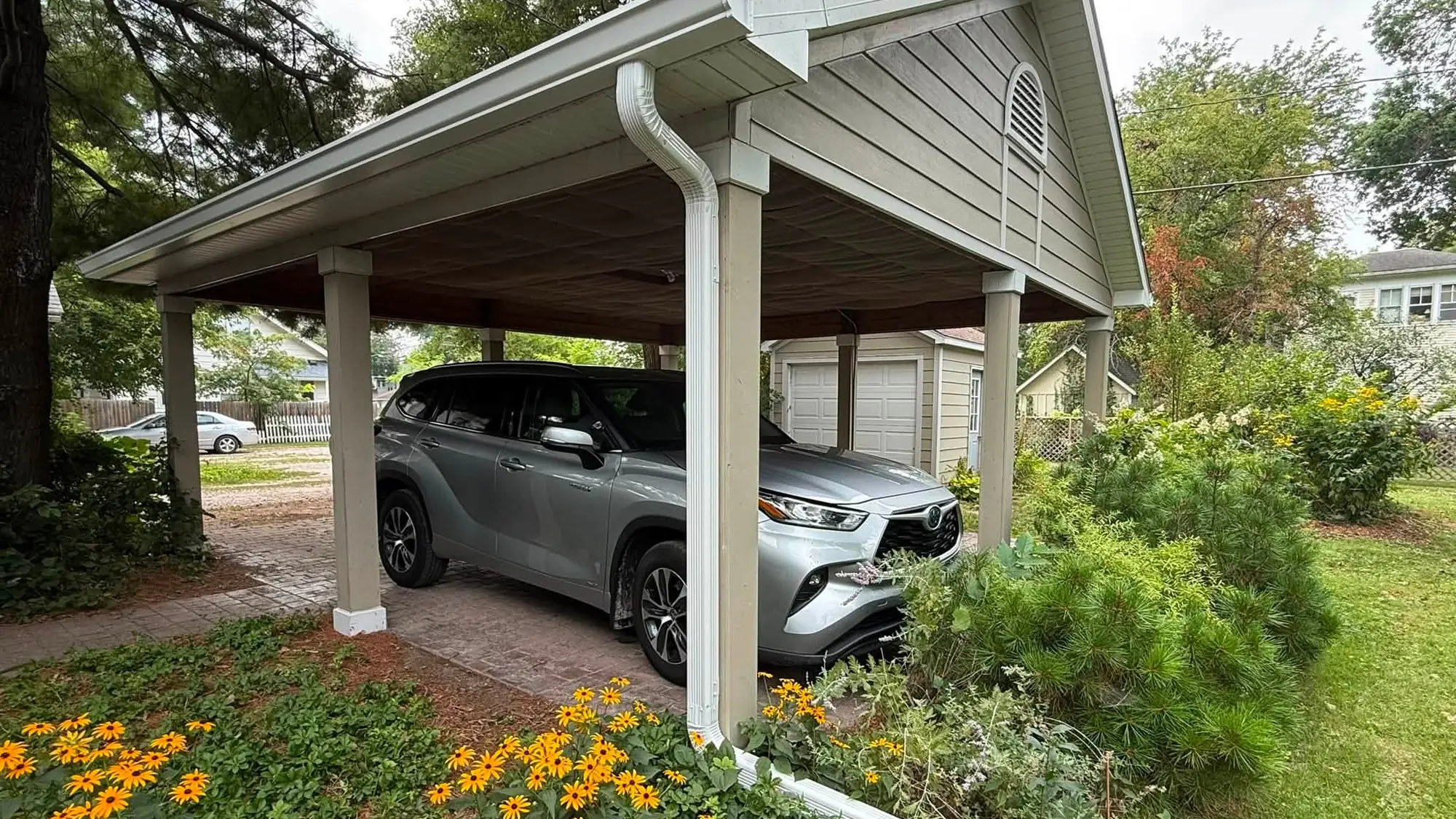 Detached carport with a new white gutter and downspout carried down past a bed of black-eyed susans