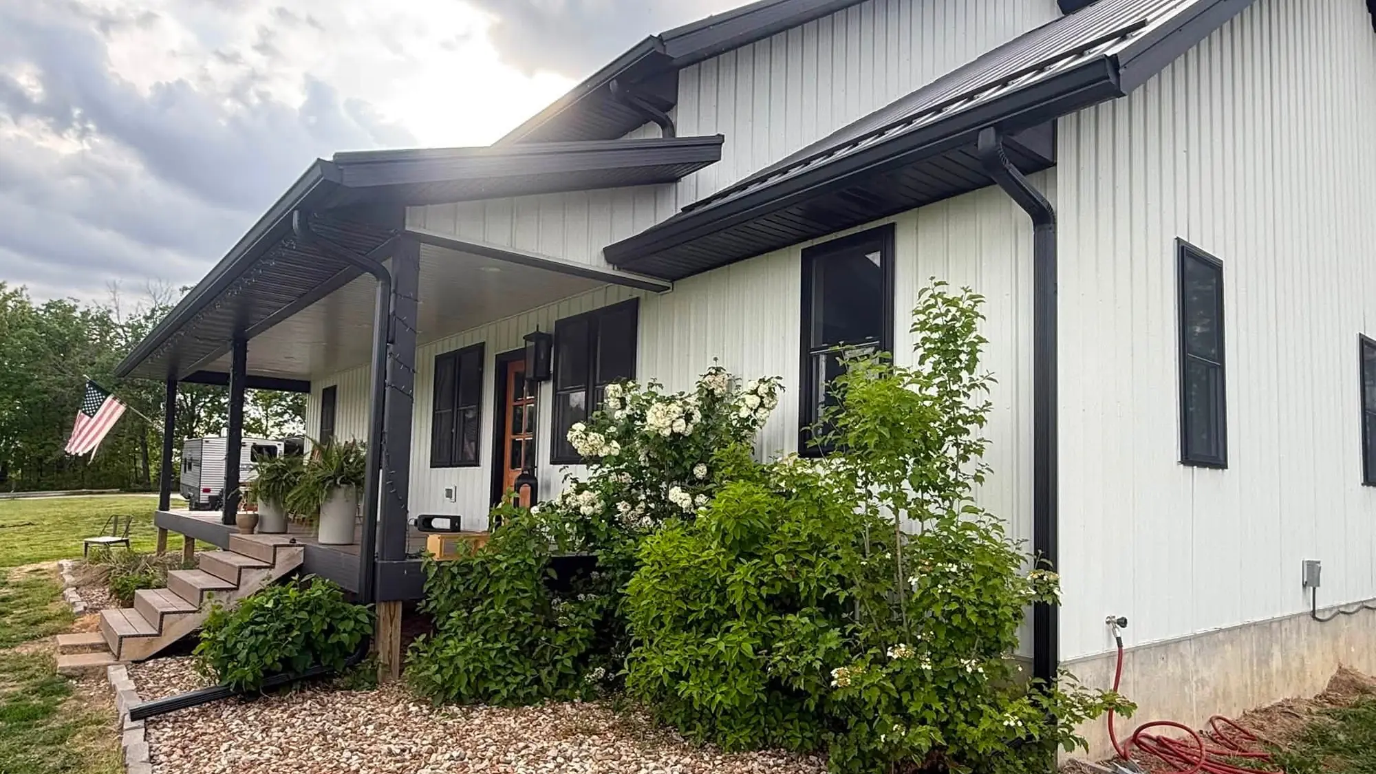 White board-and-batten home in southeast Iowa with new black seamless gutter along the porch roof