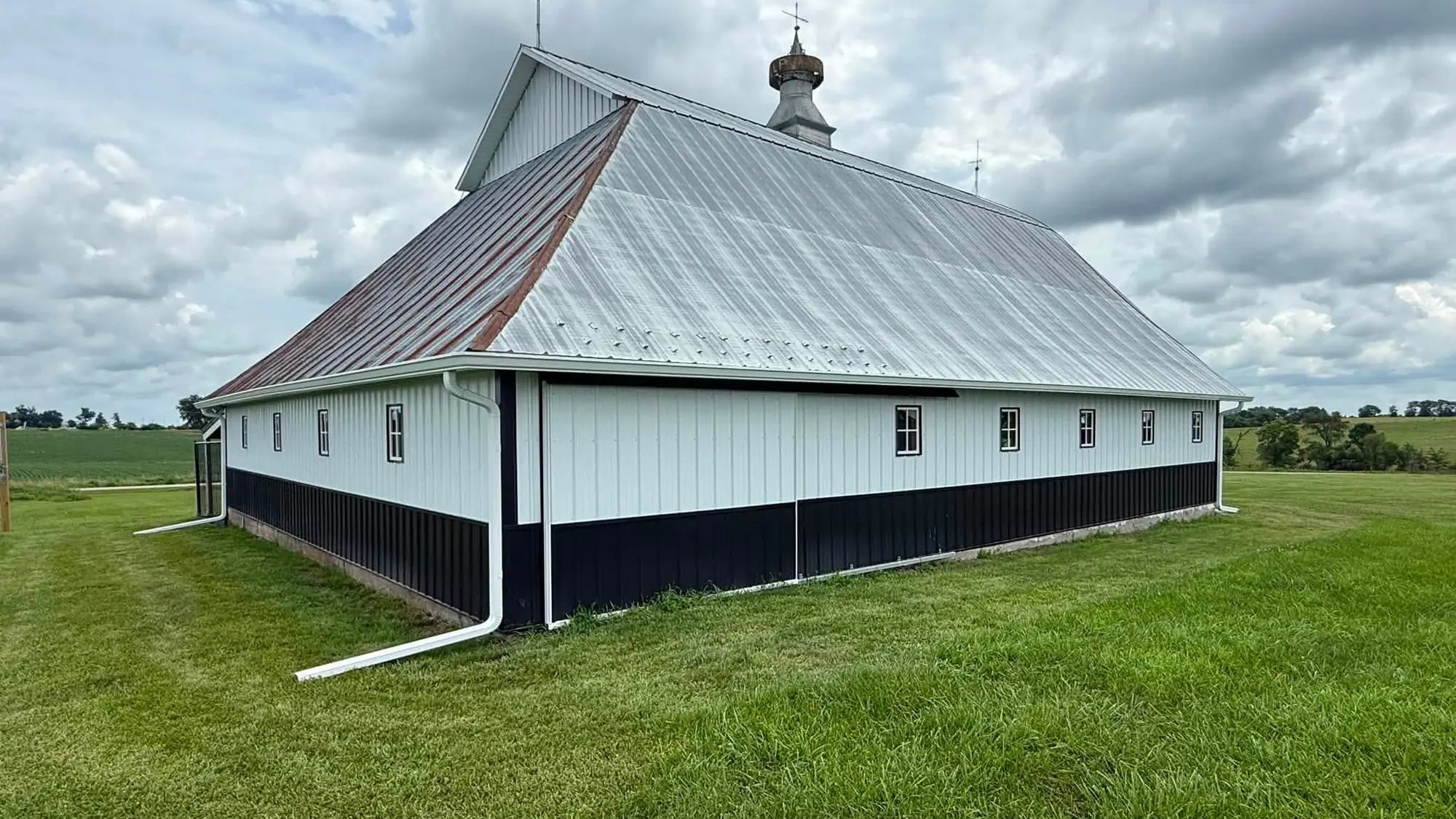 Historic white barn with a black skirt and tin hip roof, with a long white gutter run along the eave