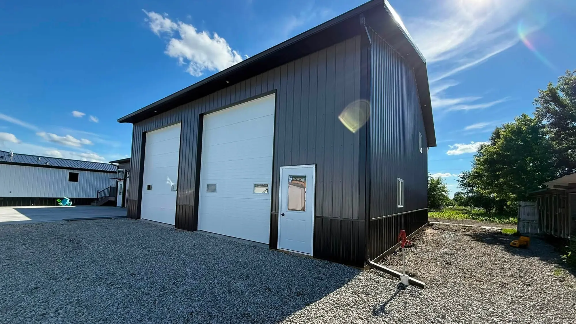 Black metal pole building with two white overhead doors and new gutter along the eave