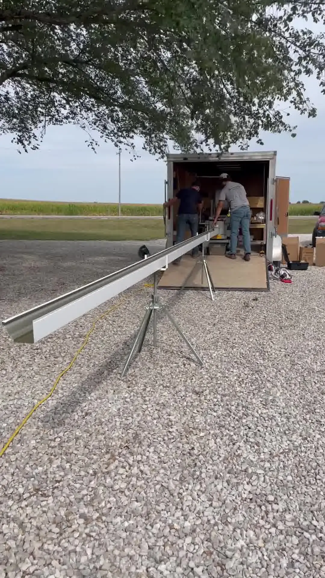 A single continuous length of white seamless gutter resting on roller stands across a gravel yard