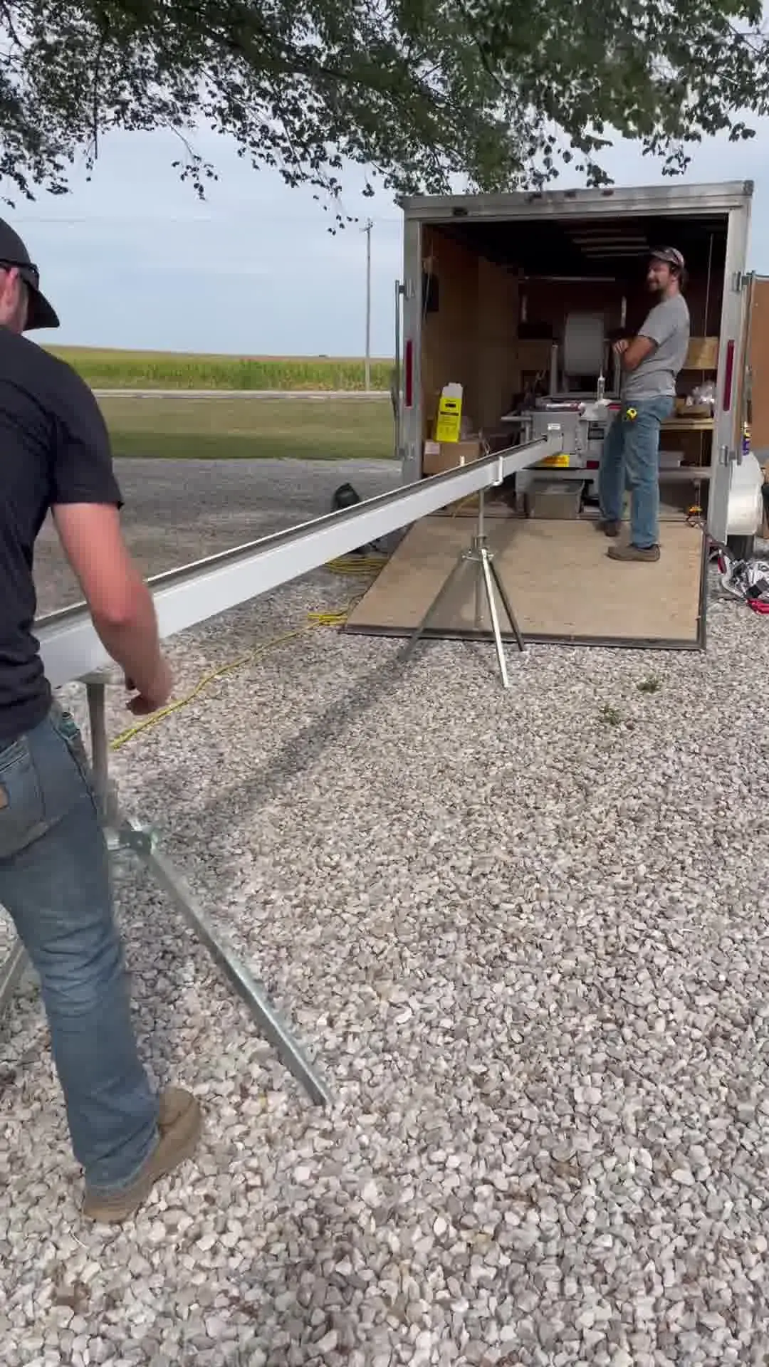 Crew member walking a freshly formed length of gutter out onto roller stands beside the company trailer
