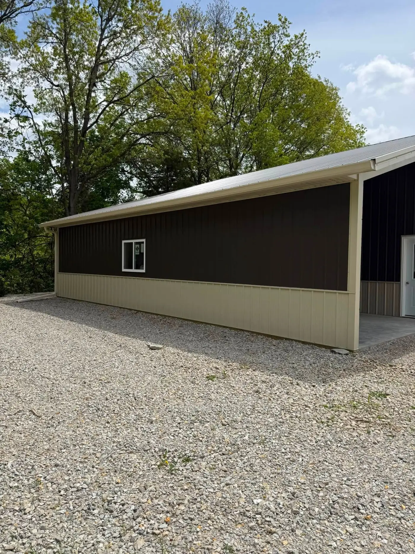 Brown pole barn with cream wainscot and cream gutter beside a tree line