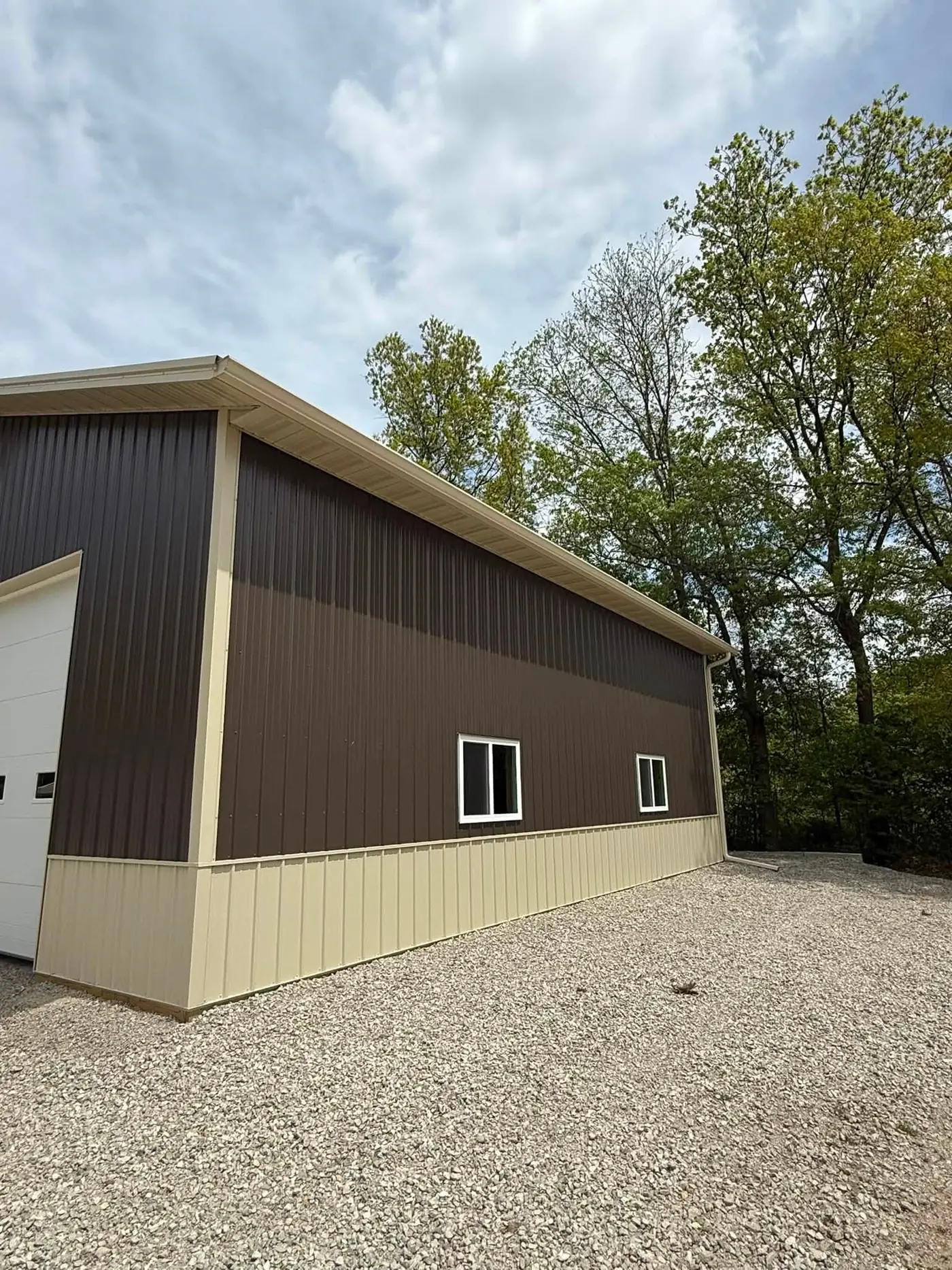 End elevation of a brown pole barn with a cream gutter along the low eave