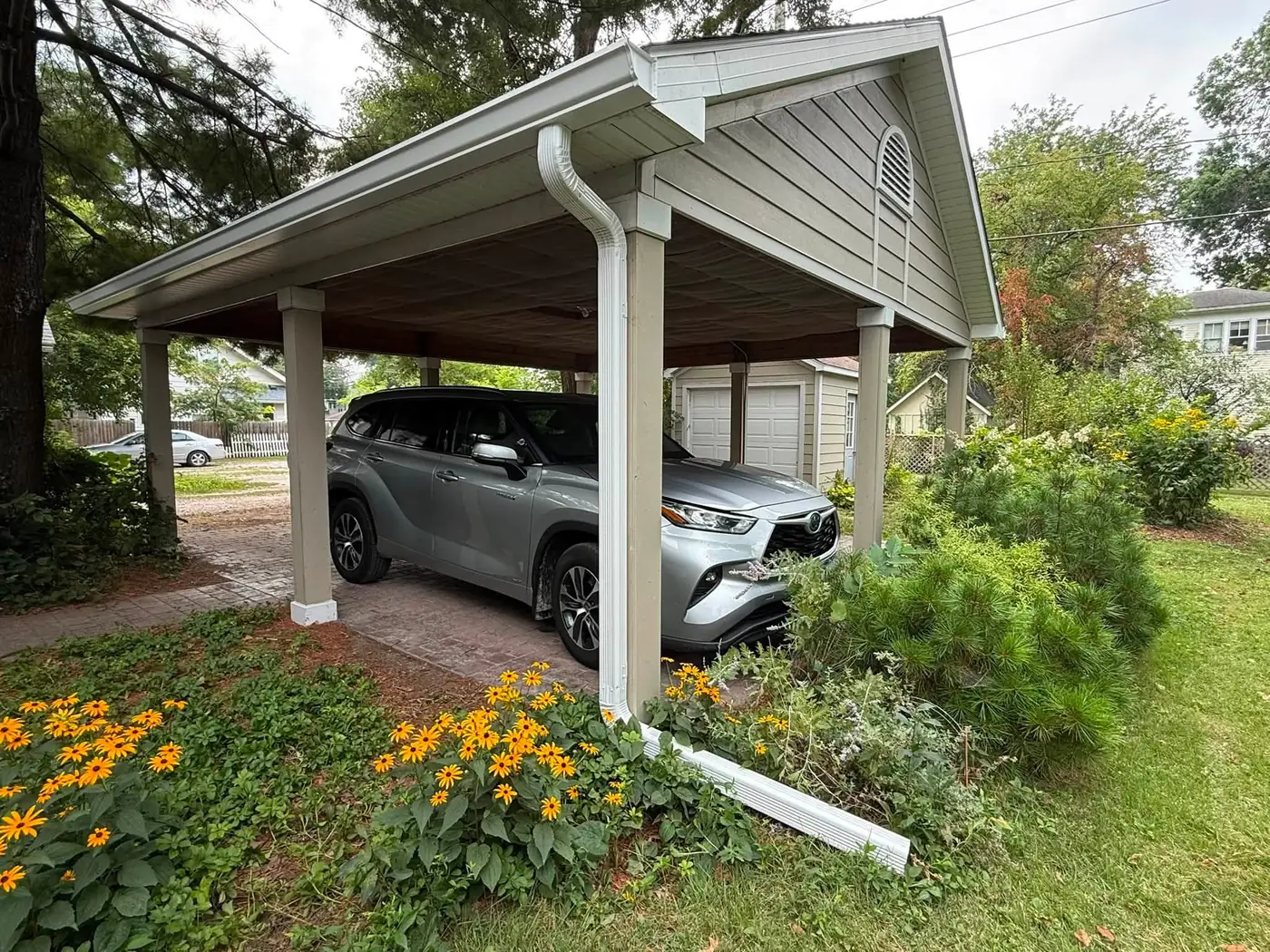 Detached carport with new white gutter and downspout beside a flower bed