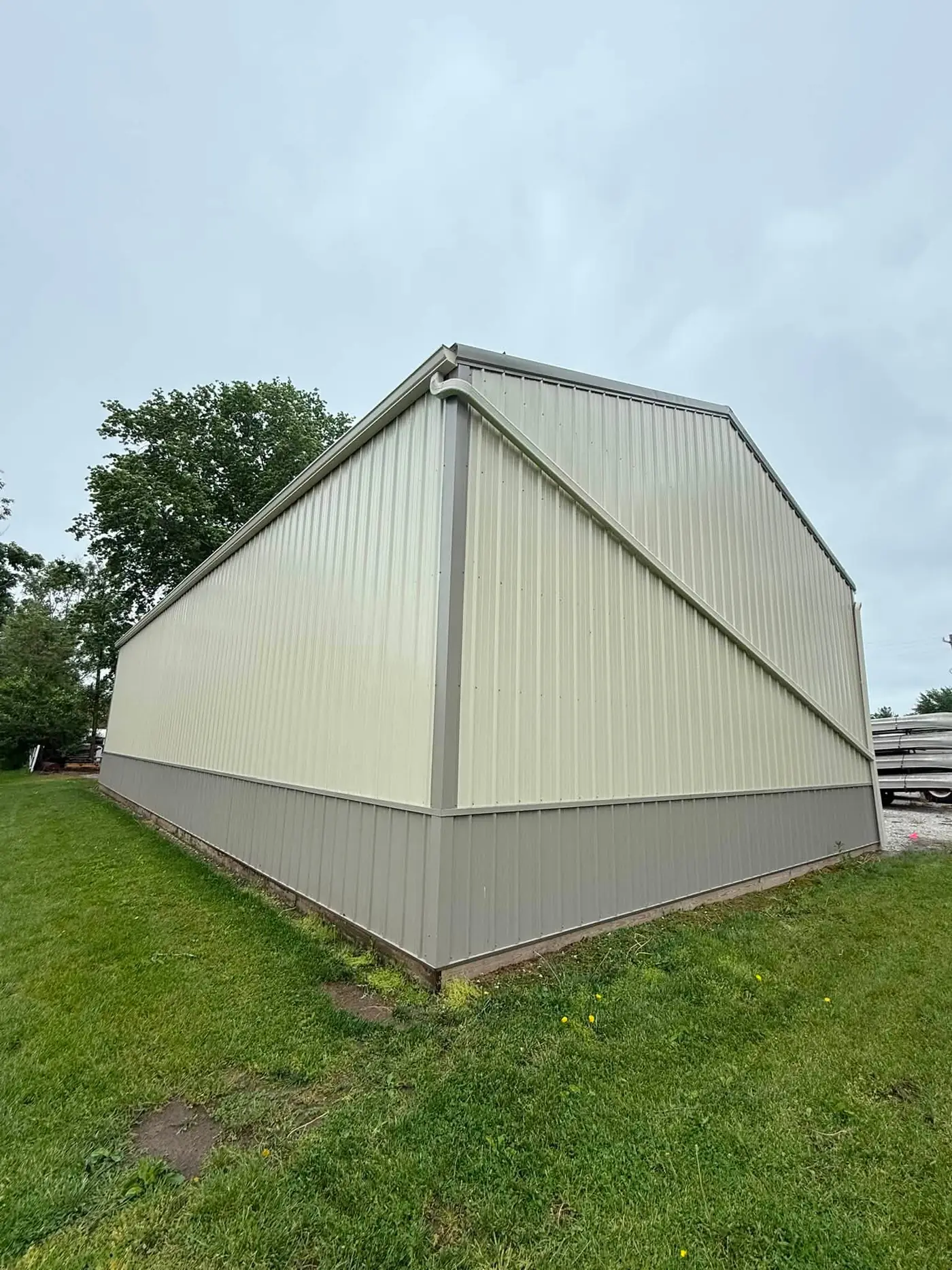 Cream pole barn gable end with gray wainscot and a gutter at the eave