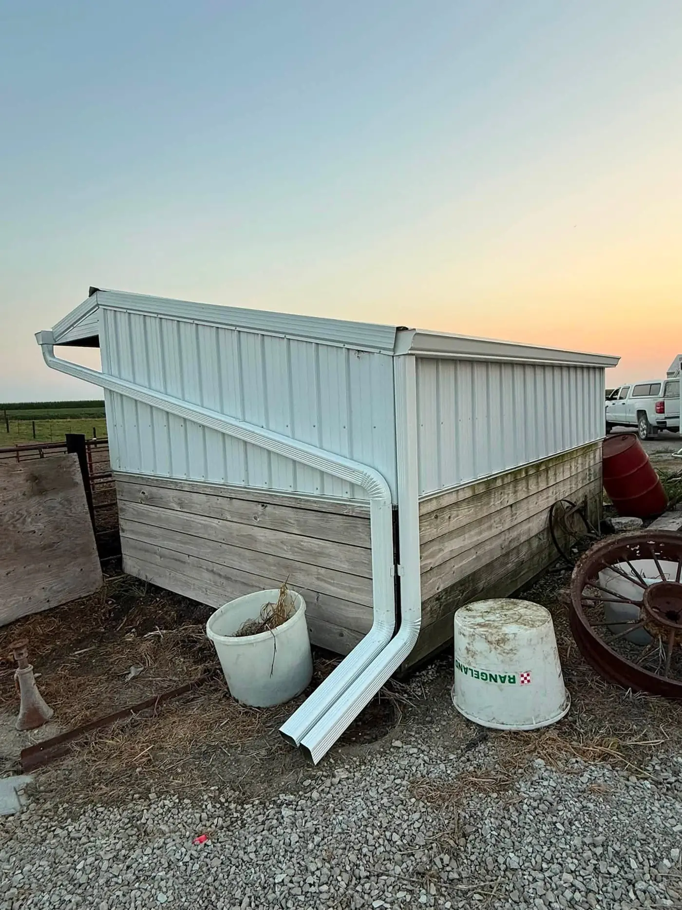 Small white farm shed at sunset with a new gutter and a long angled downspout