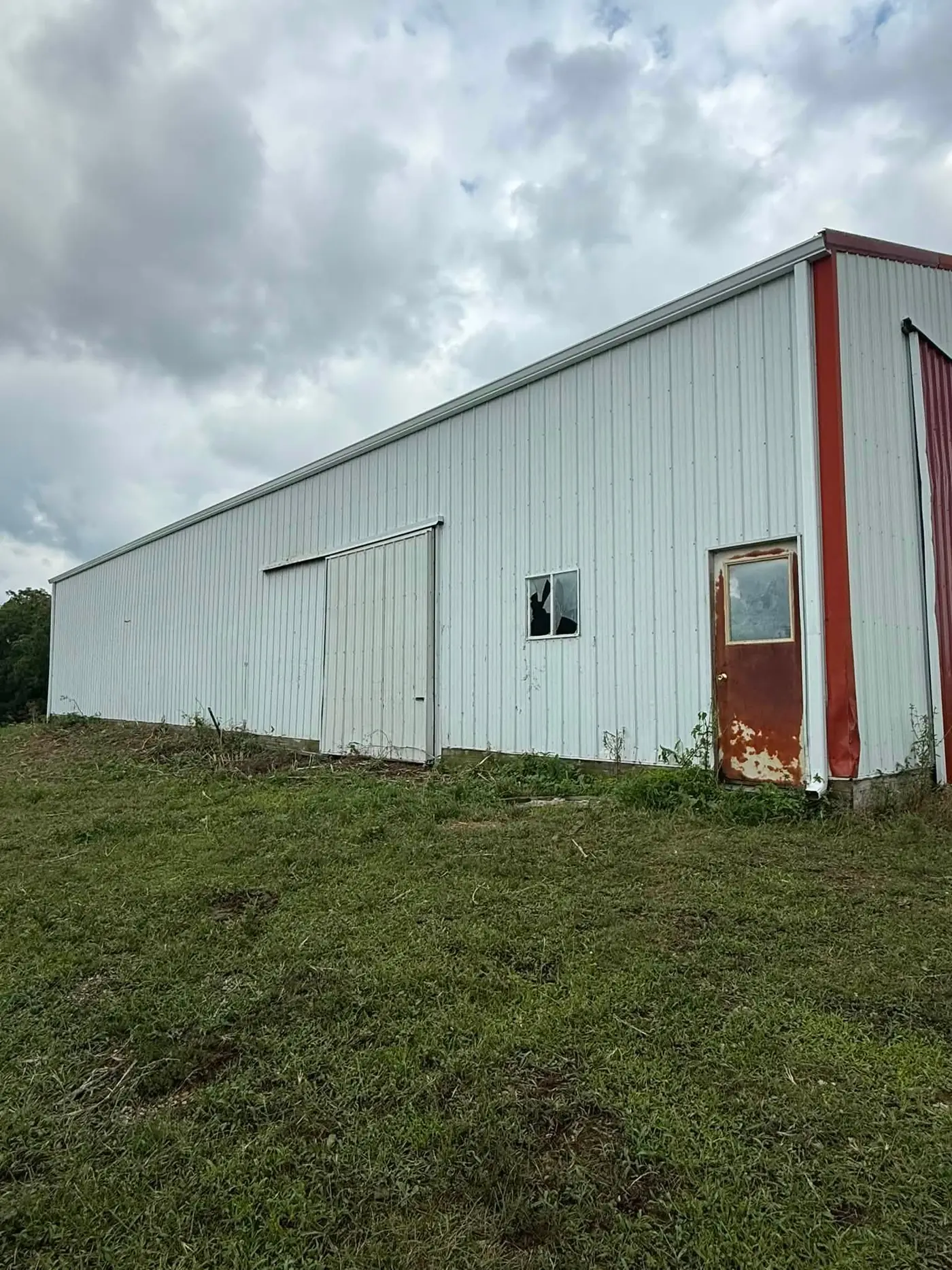Side of the weathered metal barn with a sliding door and a broken window