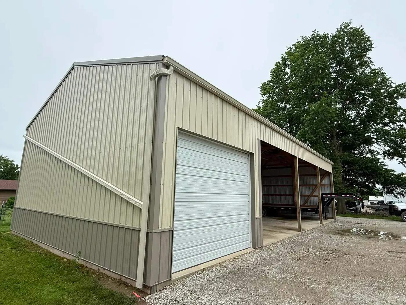Tan pole barn with a white overhead door, an open lean-to bay and a gutter along the full eave