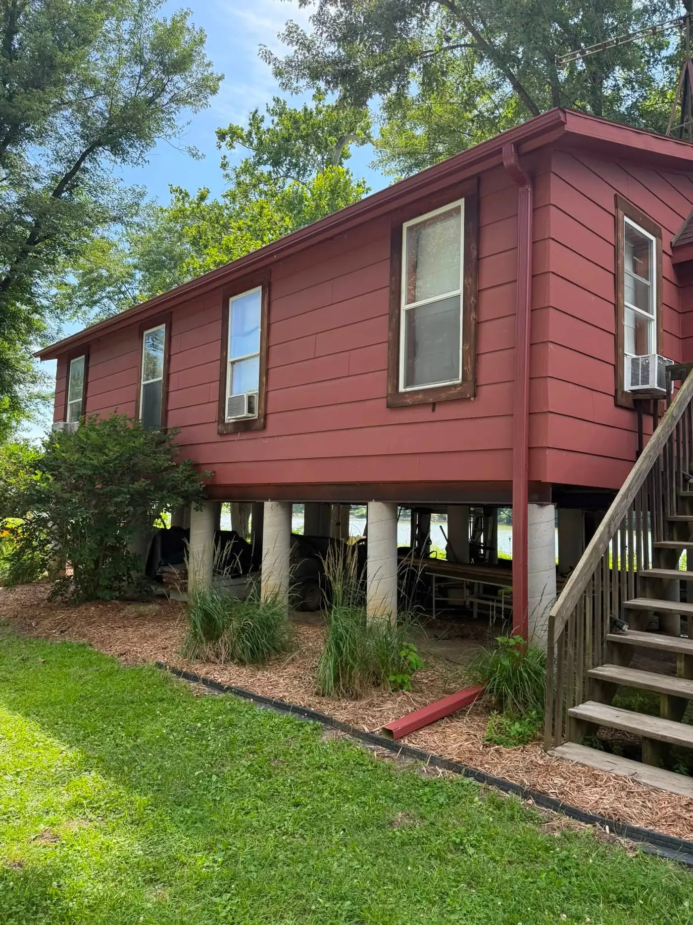 Dark red house raised on concrete piers with a gutter along the eave and a wooden stair