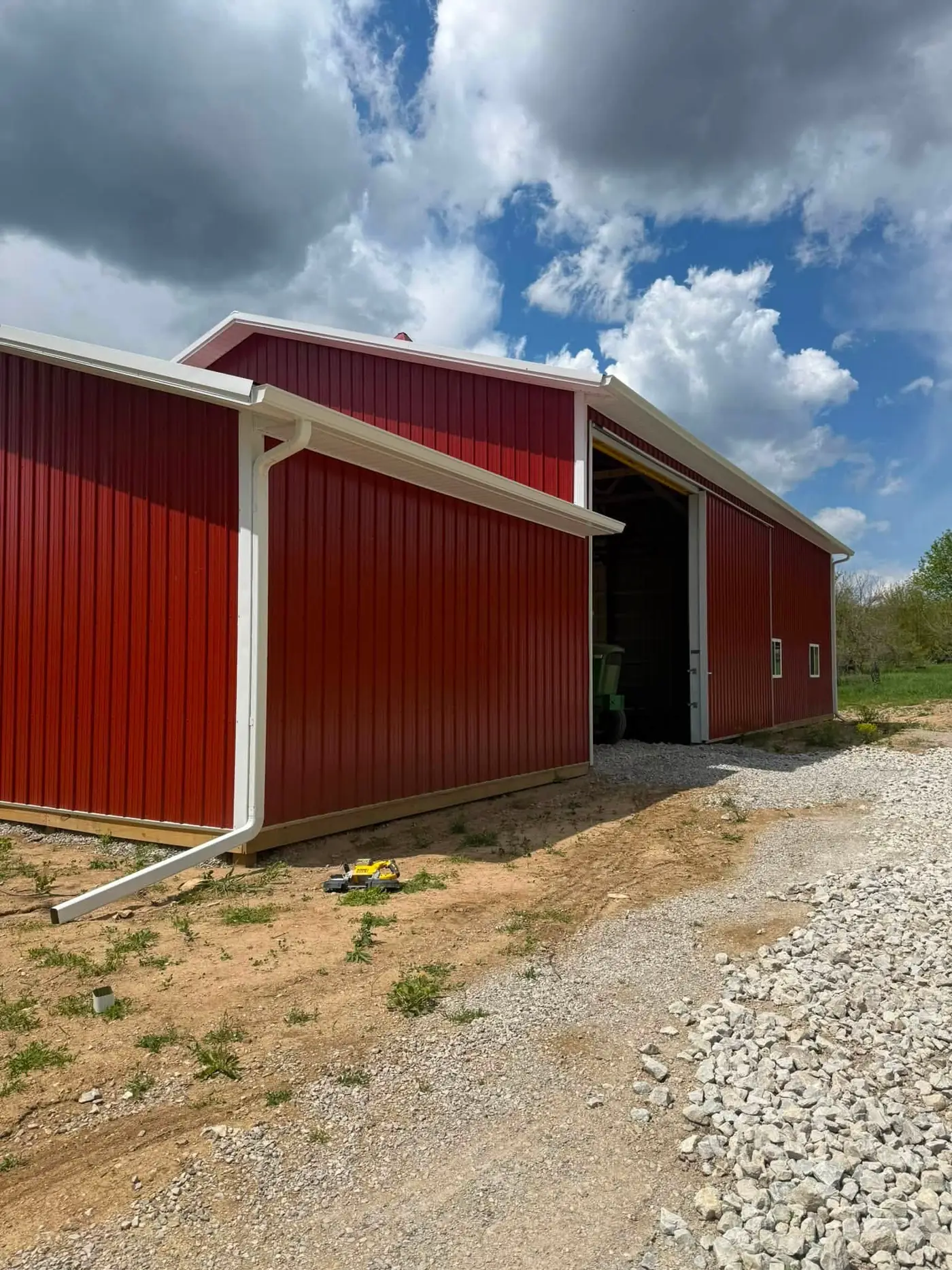 Red pole barn from the side with an open sliding door and a white gutter along the eave