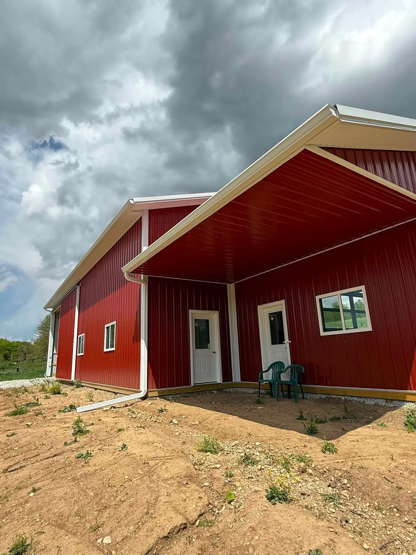 Red pole barn with white fascia and gutter under a storm sky