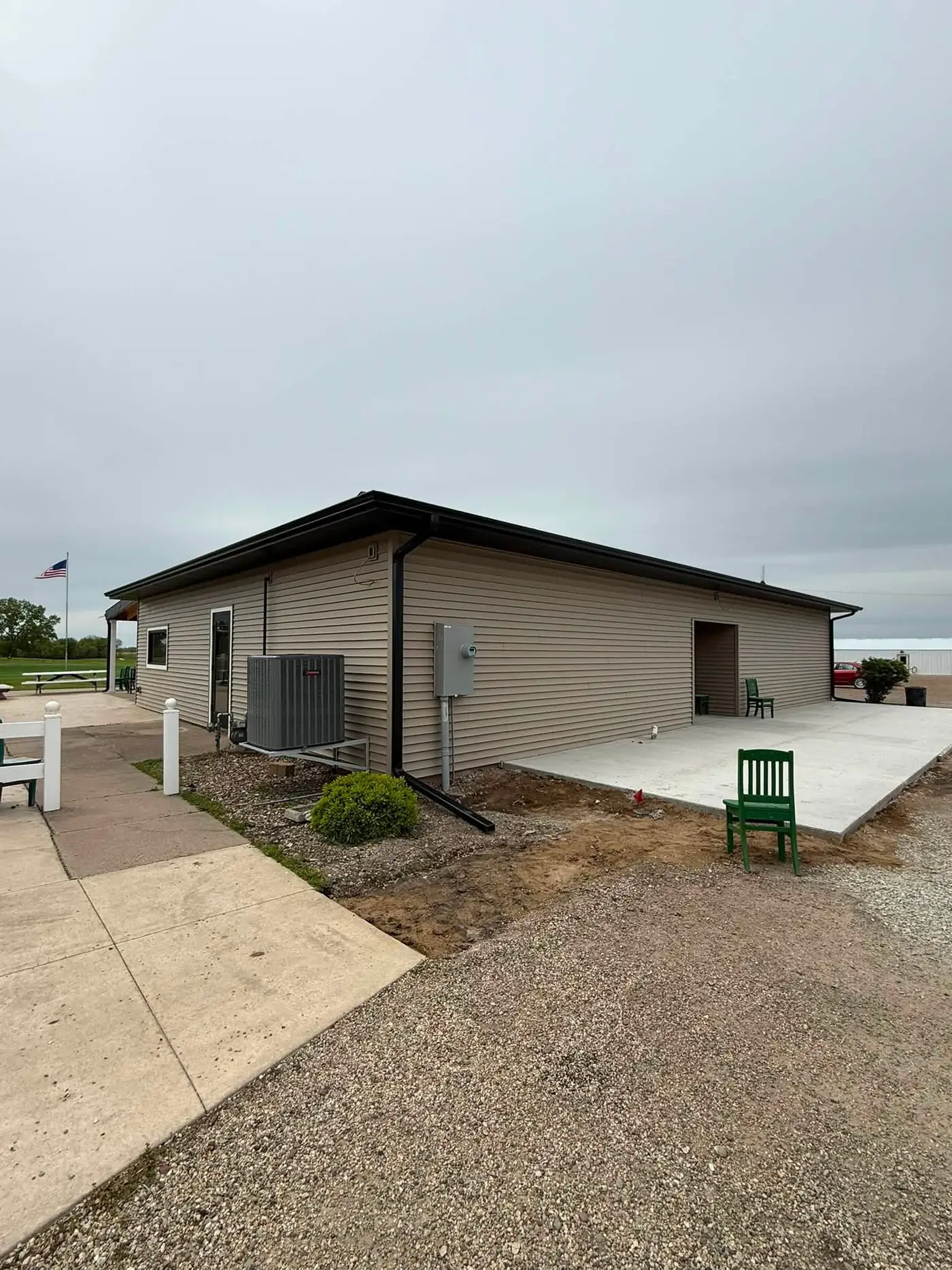 Tan shop building with a dark gutter, a wall condenser and a new concrete pad