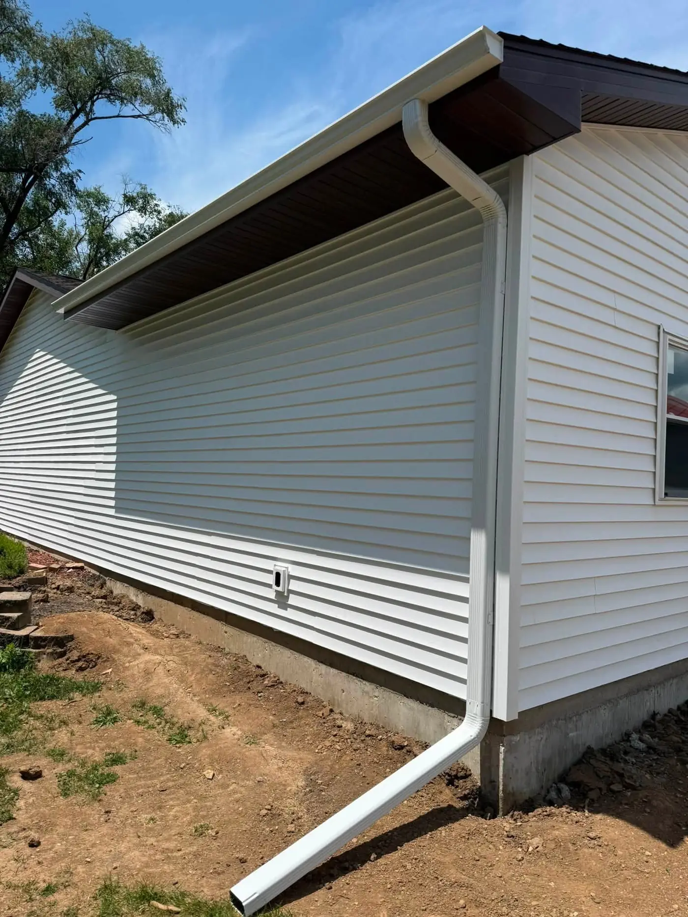 New white seamless gutter and downspout on a white vinyl-sided house under a blue sky