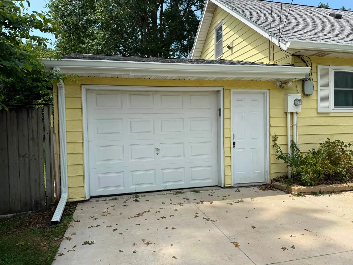 Attached garage on a yellow house with a white overhead door and a new gutter and downspout