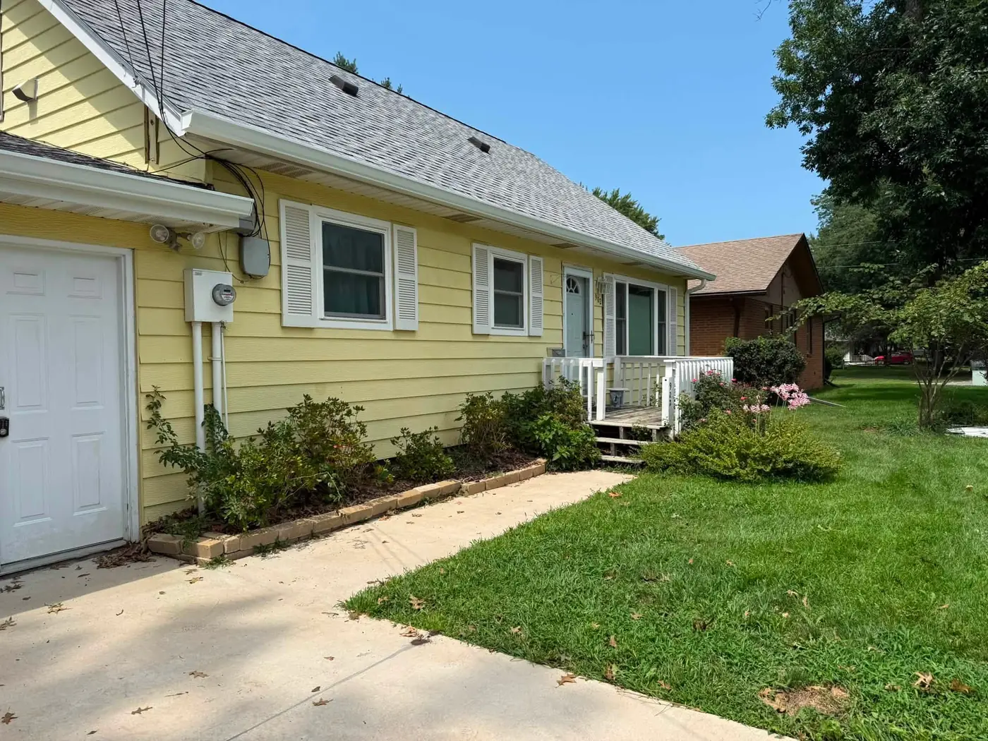 Front elevation of a yellow ranch house with a white gutter along the porch roof