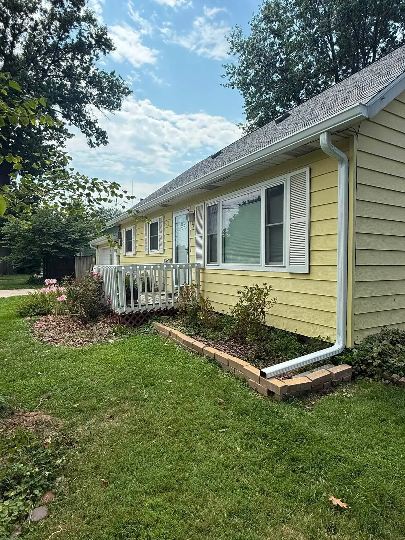 Pale yellow ranch house with a white gutter and downspout beside a deck rail