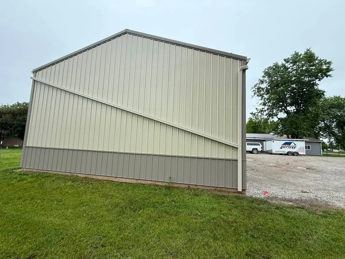 Cream pole barn with new gutter and downspout, the company trailer parked in the background