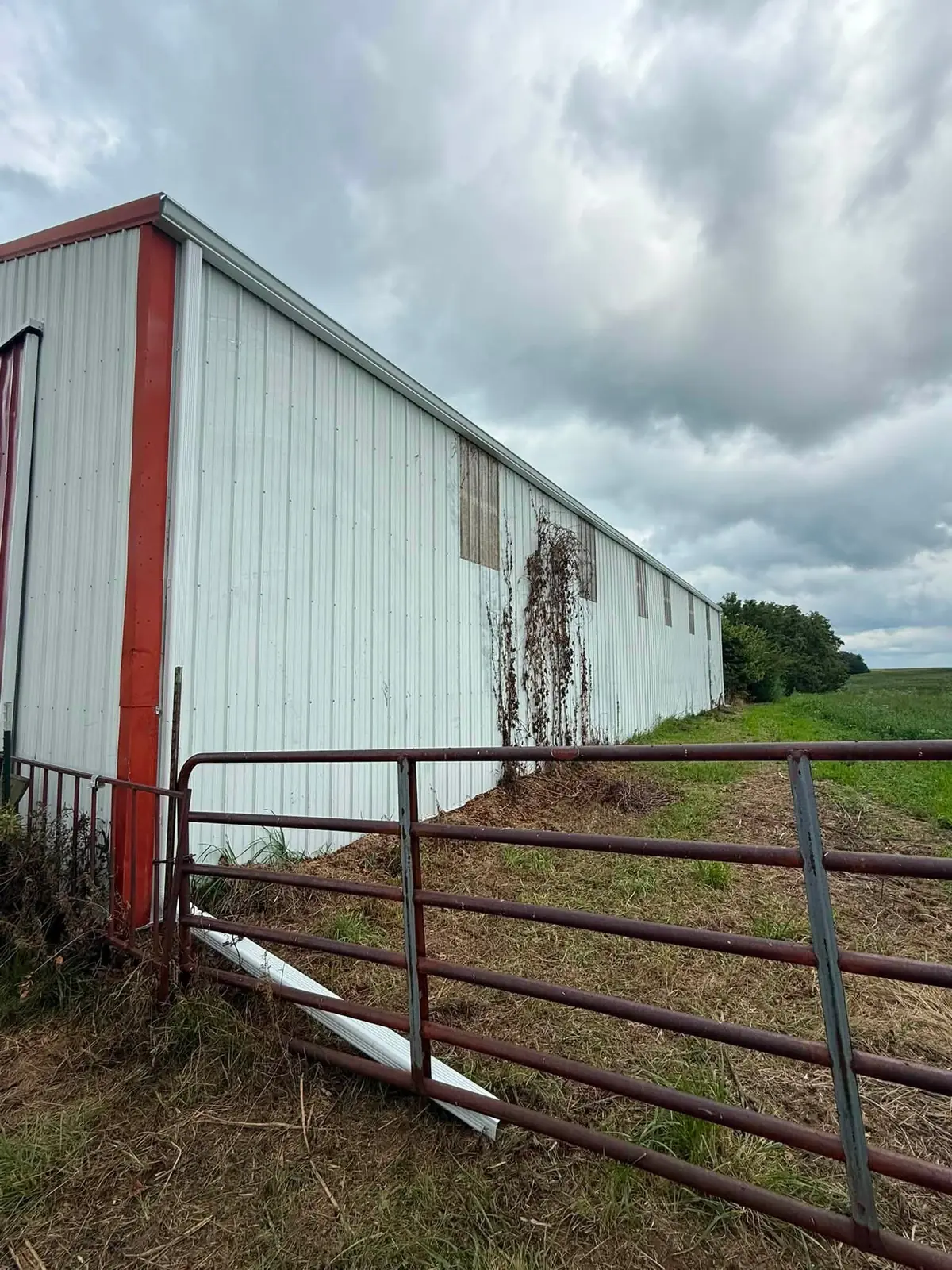 Weathered white metal barn with red trim showing rust streaking down the panels below the roof line