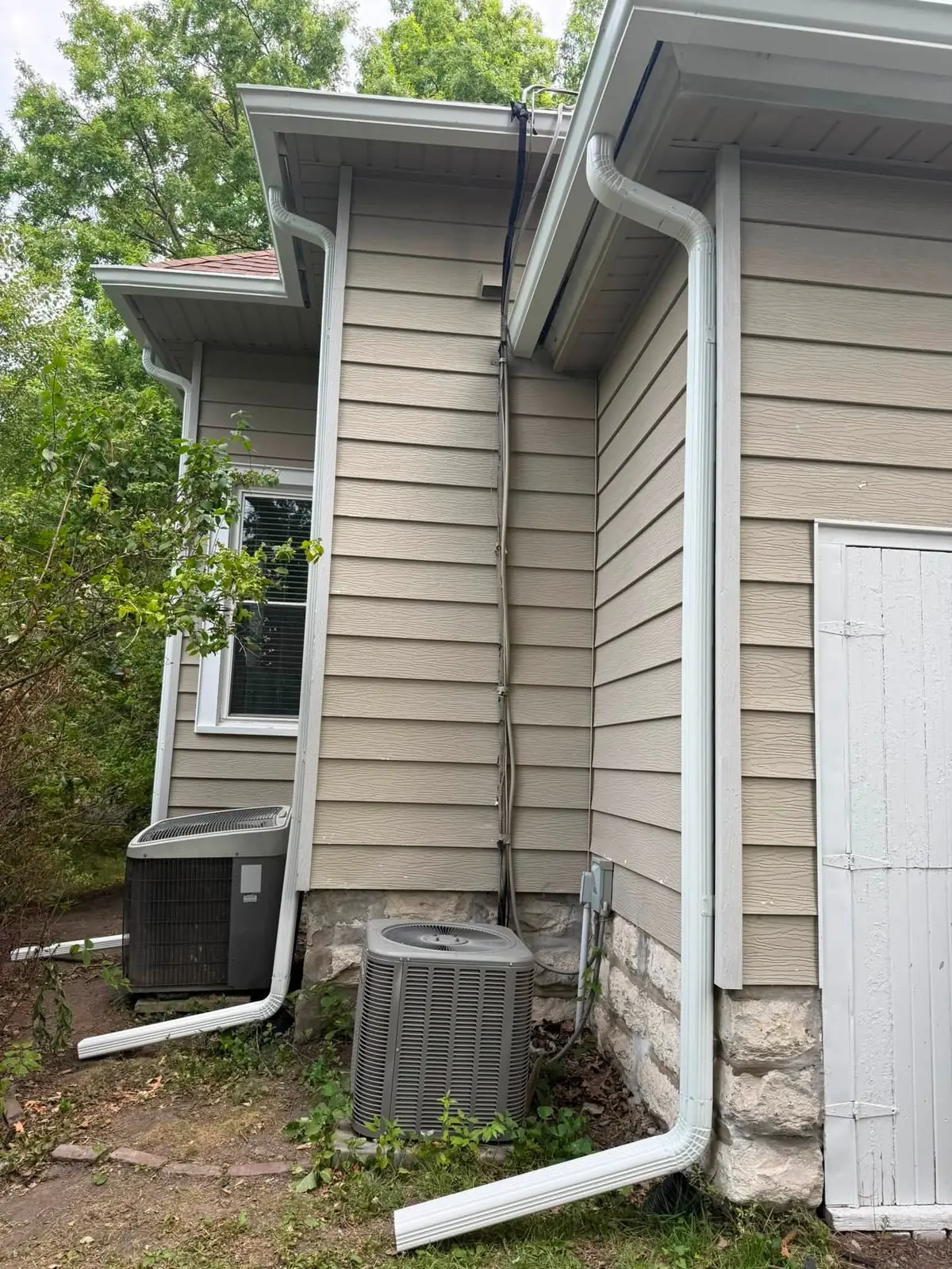 Close view of a gutter and downspout at the corner of a tan house