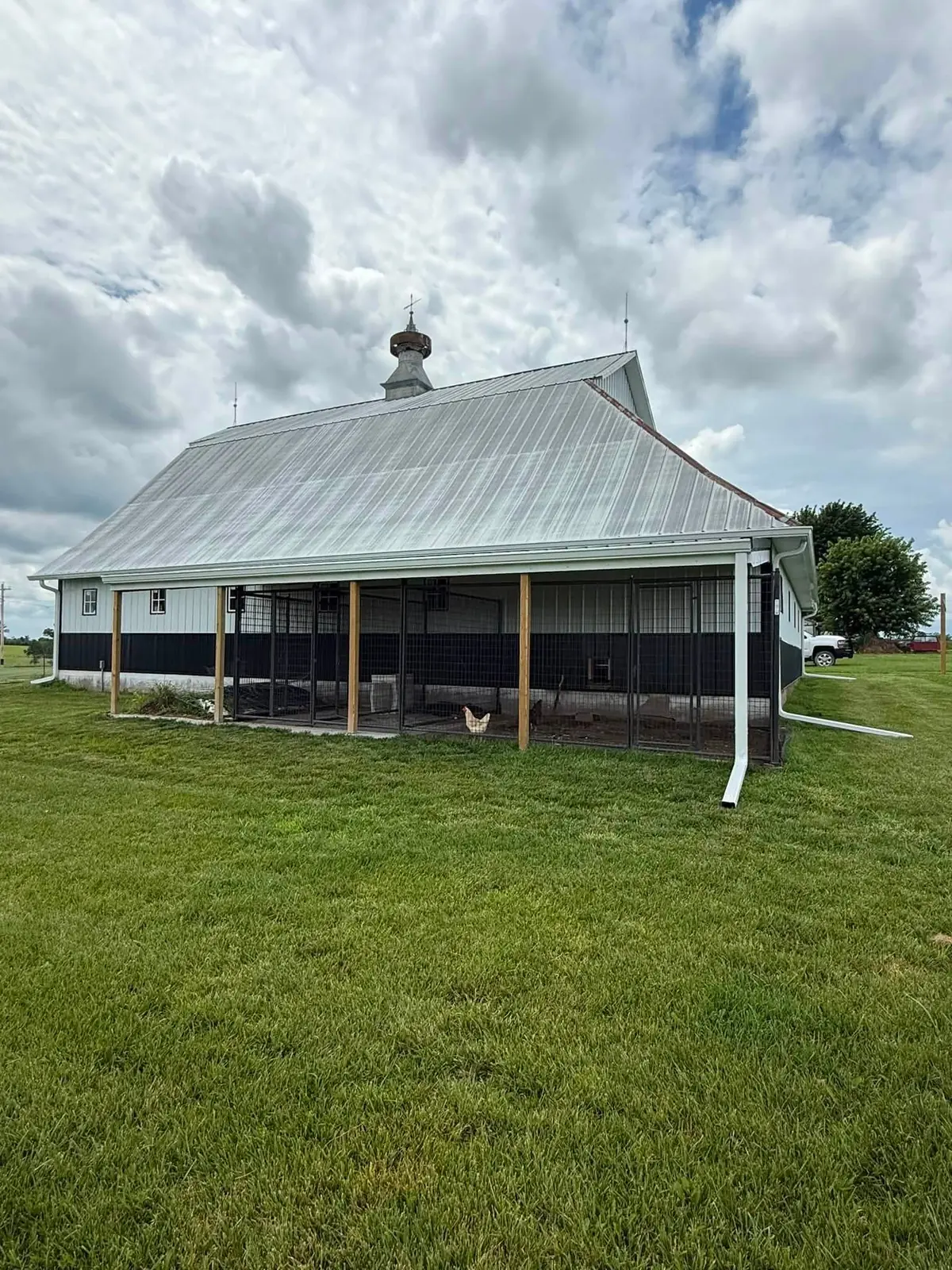 White barn with a long gutter run and two downspouts along a poultry enclosure
