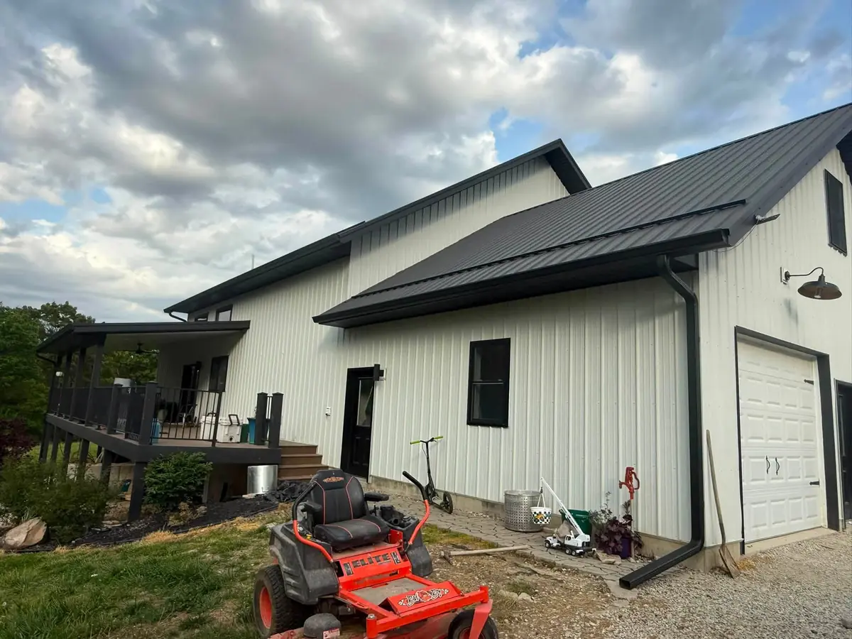White barndominium with a black standing-seam metal roof sloping down toward a deck and a garage door