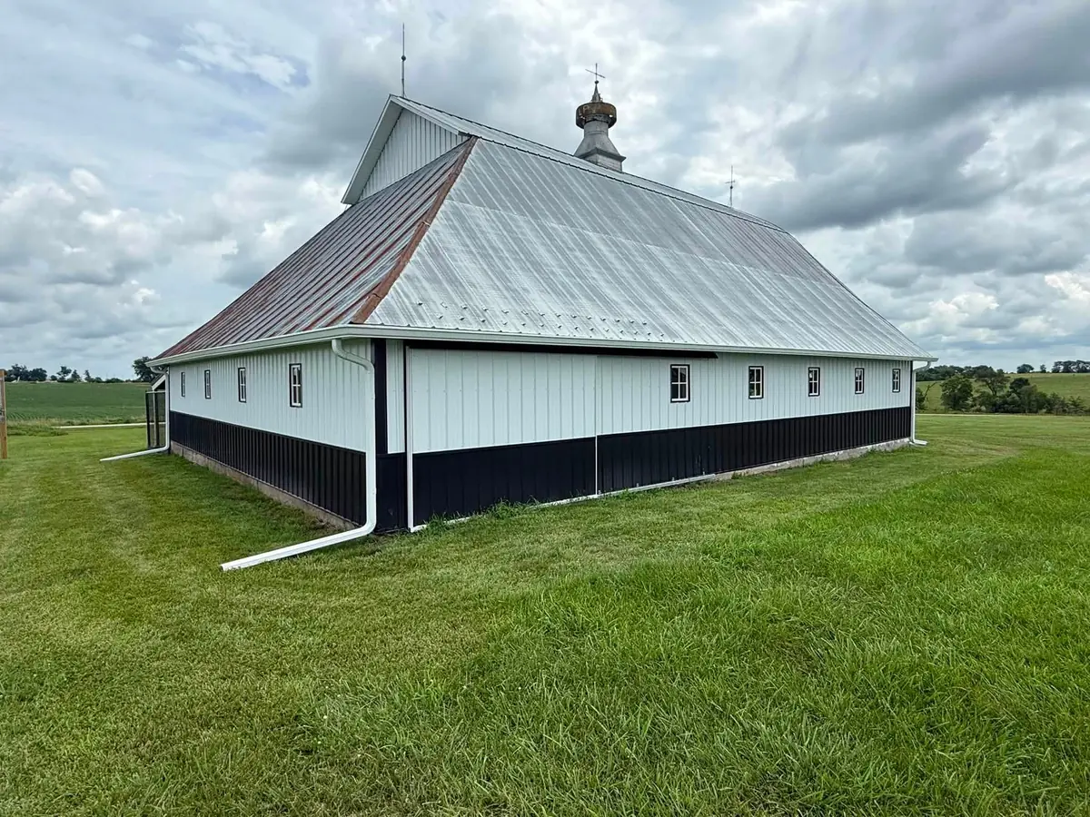 Historic white barn with a tin hip roof and cupola standing in an Iowa field, with a new white gutter along the eave
